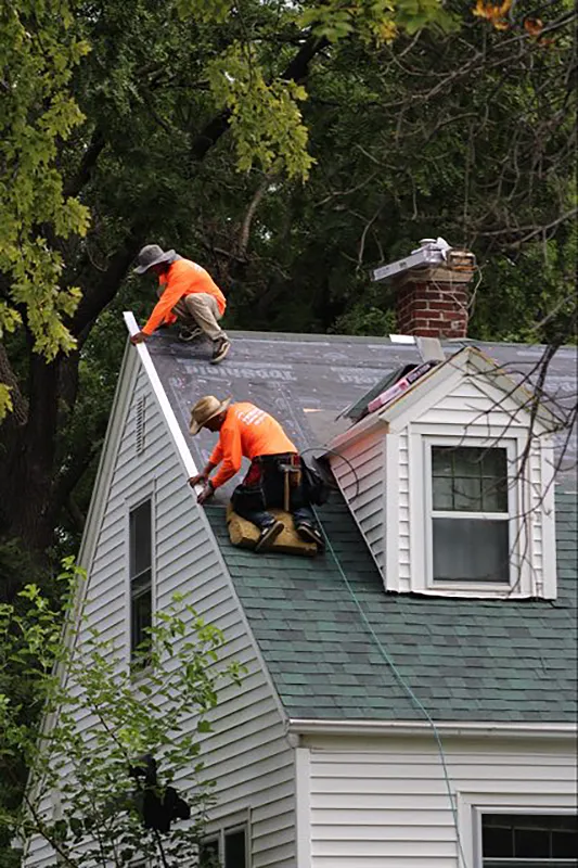 Workers on home of roof, adding shingles.